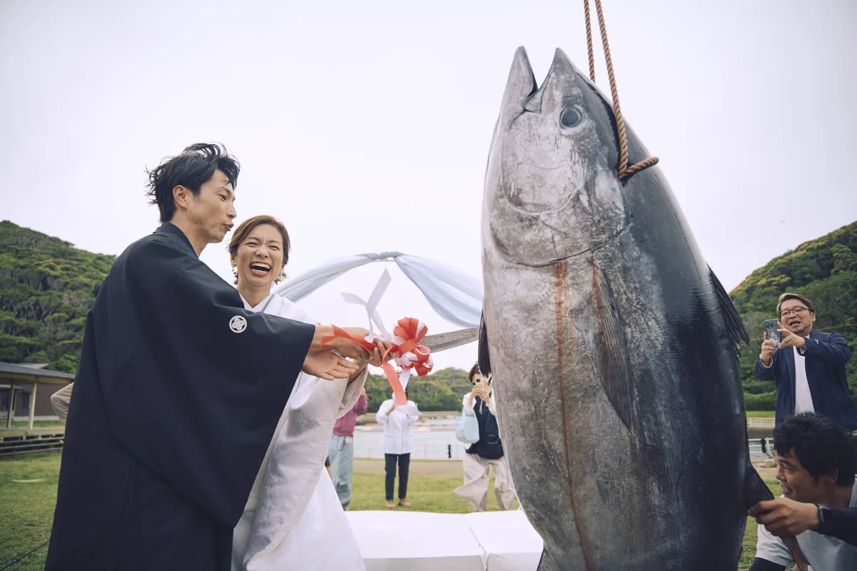 吊るされたマグロの前で笑う新郎新婦