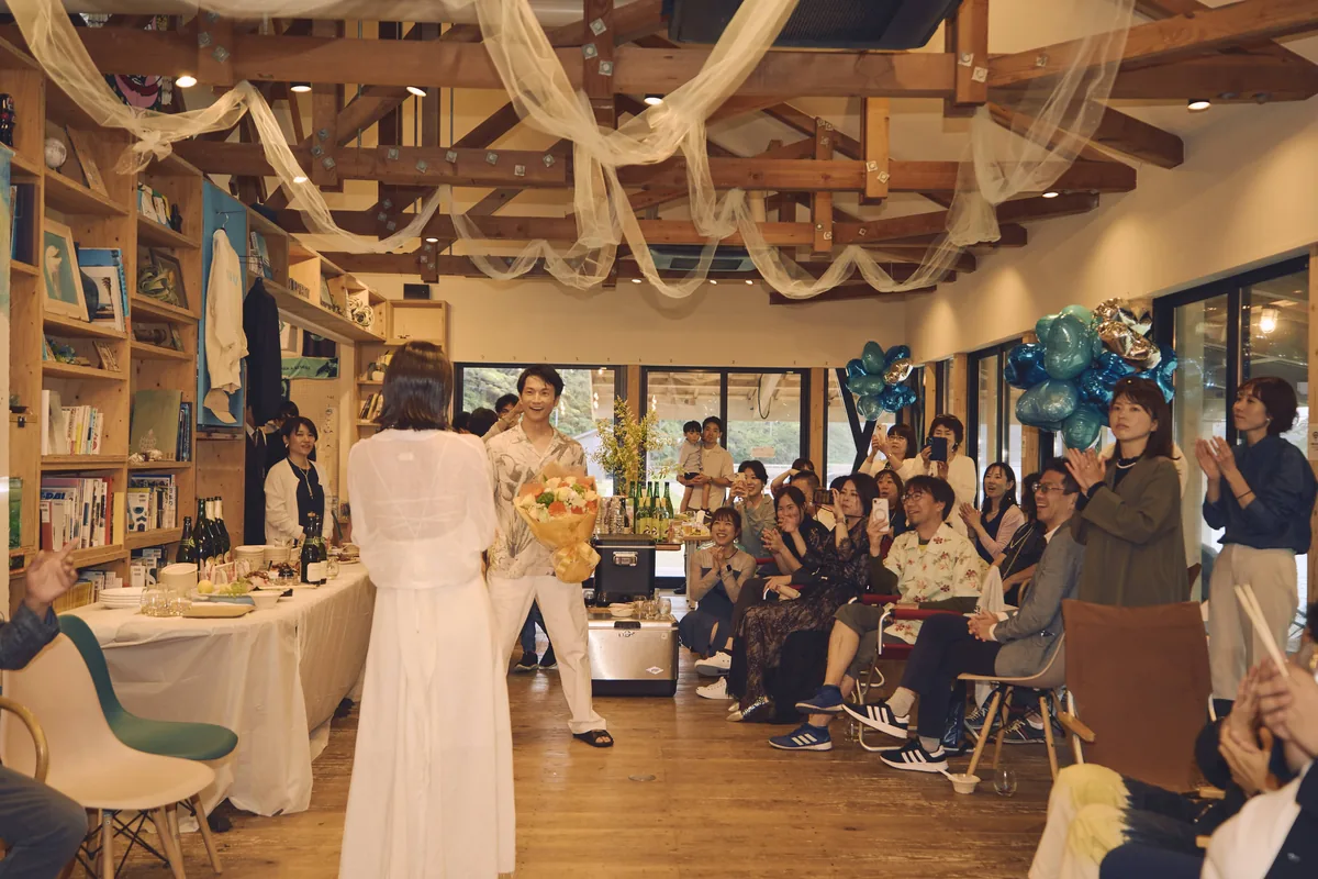 梁に布を渡して飾った屋内の会場で、ゲストに囲まれる新郎新婦